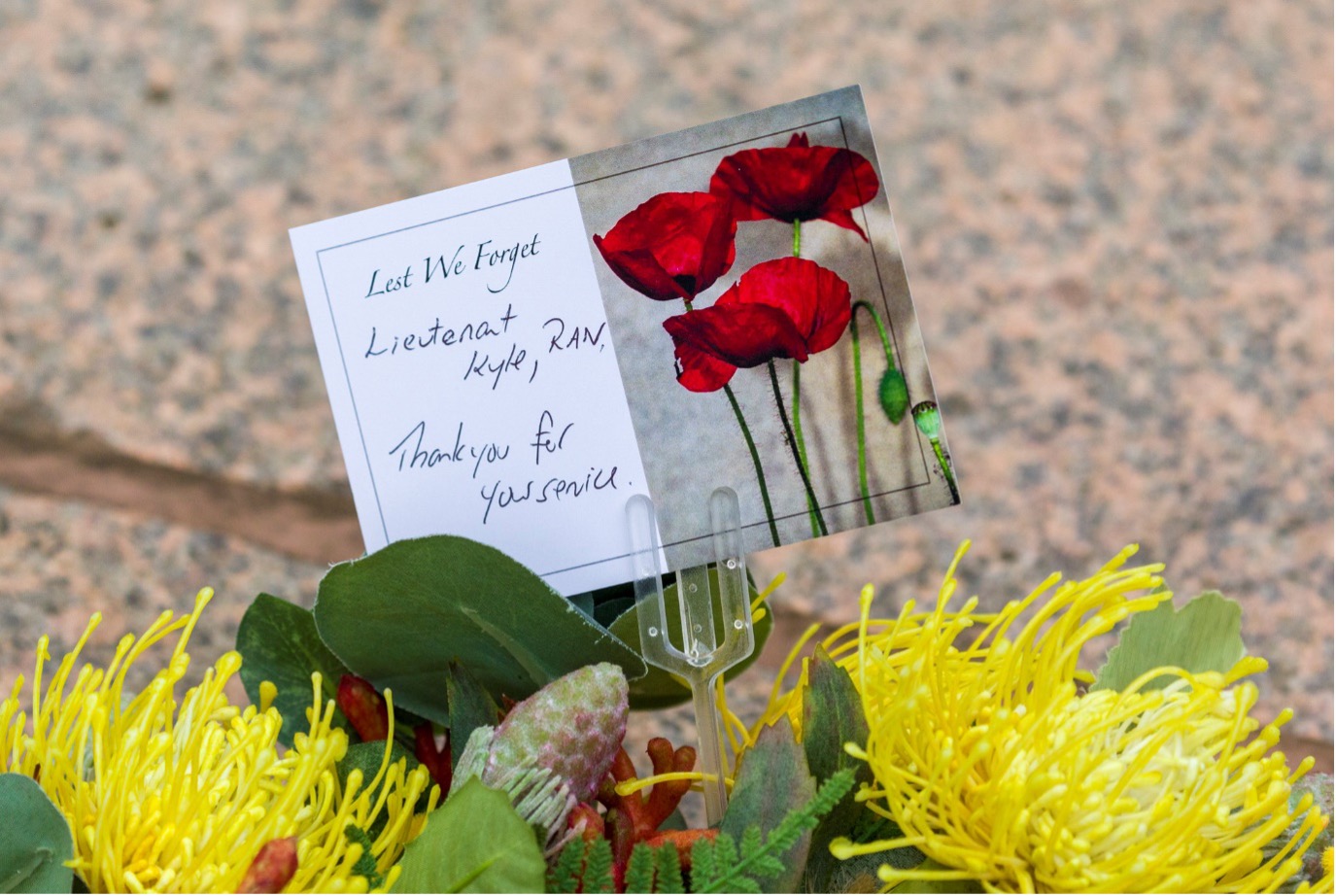 Card on floral wreath with message, ‘Lest We Forget. Lieutenant Kyle, RAN. Thank you for your service.’ (Australian War Memorial)