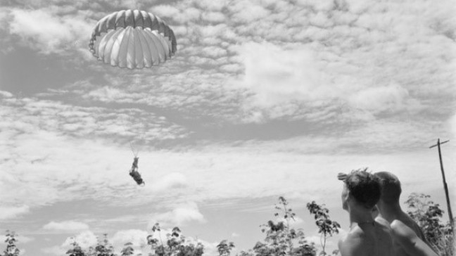 Two unidentified soldiers from 3rd Battalion, The Royal Australian Regiment (3RAR), watch as supplies float down via parachute to the landing zone (LZ) of their forward company base. As no roads link the forward bases, all supplies have to be airlifted or brought in by helicopter.