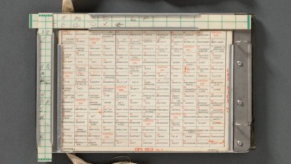 Manual cipher device with a grid in the centre with words in each cell and sliding rulers along the top and side.